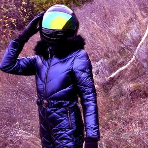 WALKS IN THE SCAFANDER IN ANCIENT RUINS. BLUE SHINY WINTER JUMPSUIT WITH HOOD AND BLACK HELMET